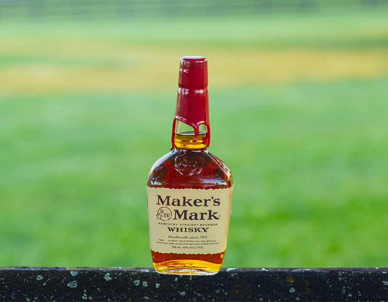 Photo of a Maker's Mark Kentucky Bourbon bottle on a rustic wooden fence in rural Kentucky.